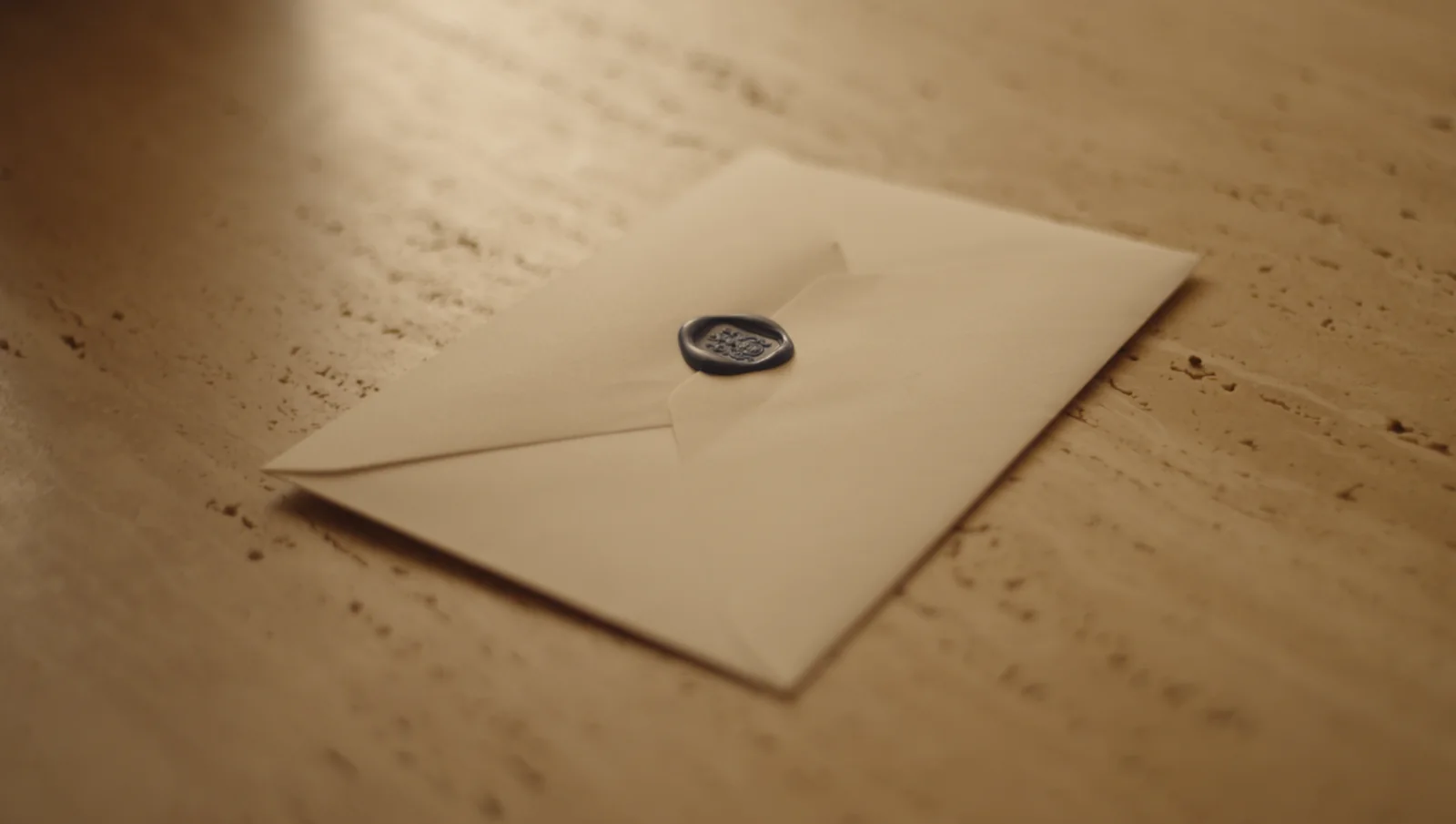 A sealed envelope with a dark wax seal on a stone table.