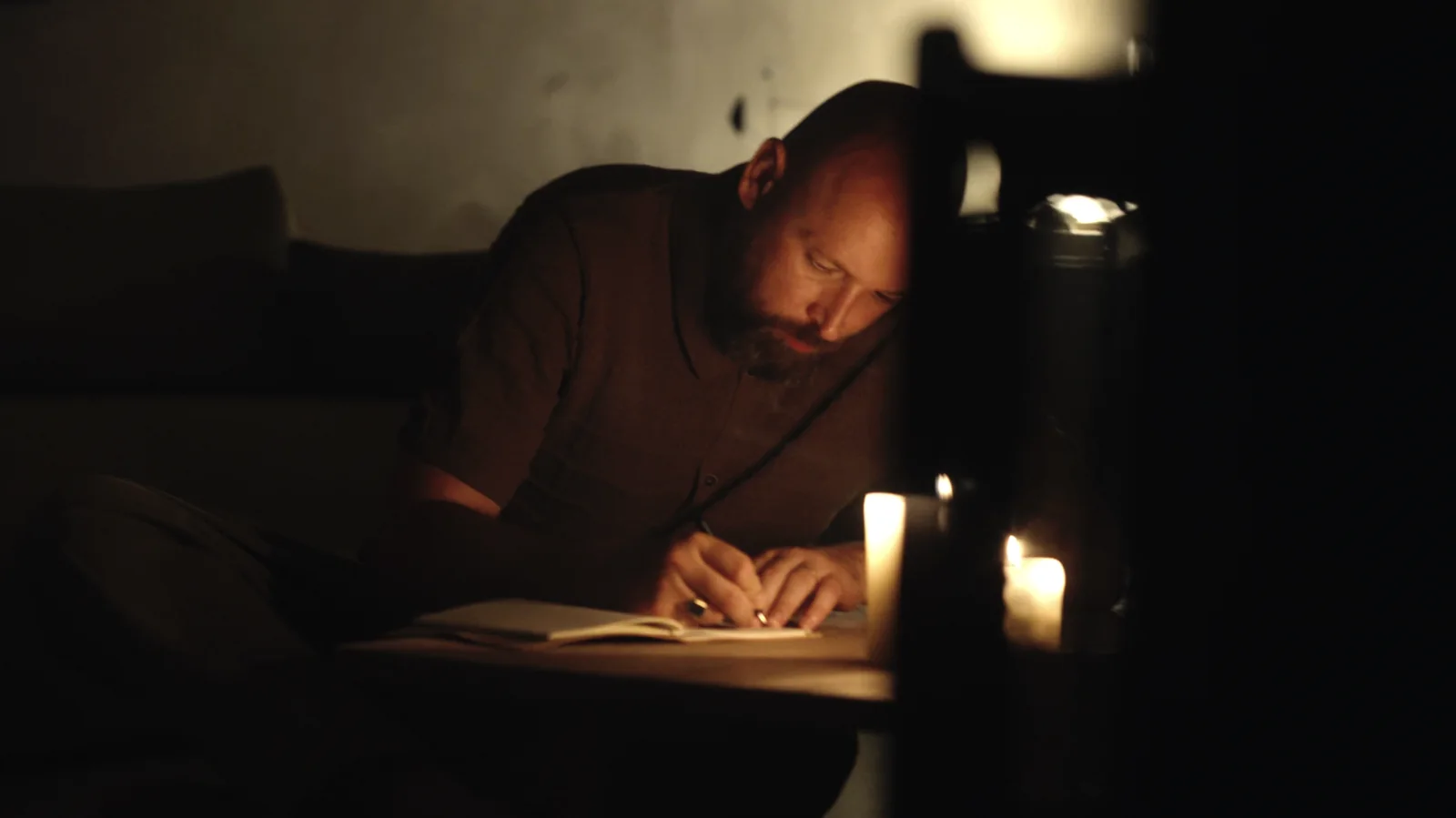 A man writing in a booklet by candlelight.